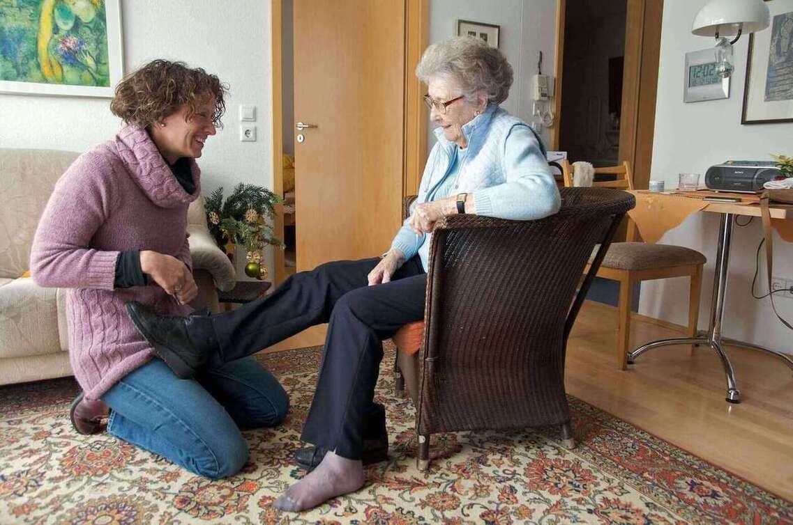 Woman helping an elderly woman helping her to tie her shoes up